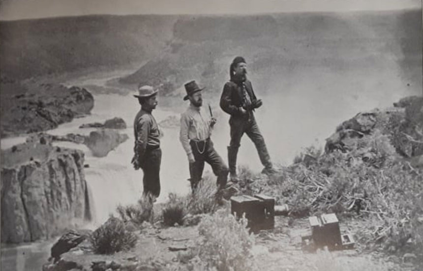 Two unidentified men stand to the right of artist Thomas Moran